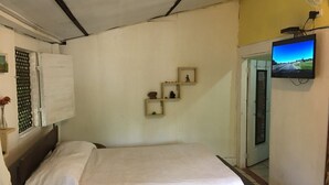 Une chambre à coucher avec un lit, un téléviseur fixé au mur et une petite étagère ornée d’objets décoratifs.