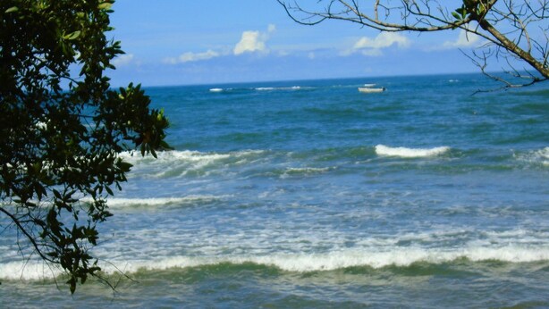Une vue sur l’océan, avec des vagues et un bateau au loin.
