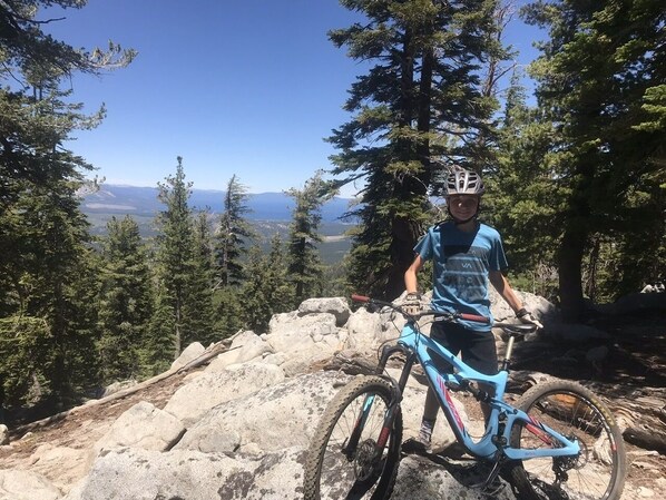 Un ciclista da mountain bike su un sentiero roccioso, con vista libera su montagne e alberi lontani.