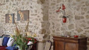 A room with a stone wall, a wooden cabinet, a bed with blue and white pillows, and a vase with flowers. - Facing the valley, in Ste Jalle, gîte equipped for 4 (Sainte-Jalle)