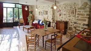 A cozy living room with a stone wall, wooden furniture, and a large window. - Facing the valley, in Ste Jalle, gîte equipped for 4 (Sainte-Jalle)