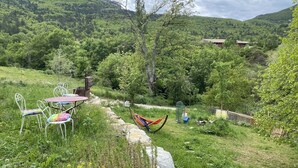 A lush green landscape with a hammock, a table with chairs, and a small building in the background. - Facing the valley, in Ste Jalle, gîte equipped for 4 (Sainte-Jalle)