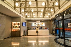 A hotel reception area with a modern design, including a reception desk, a digital screen, and a glass entrance.