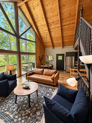 A spacious living area with a high ceiling, large windows, and a modern kitchen.