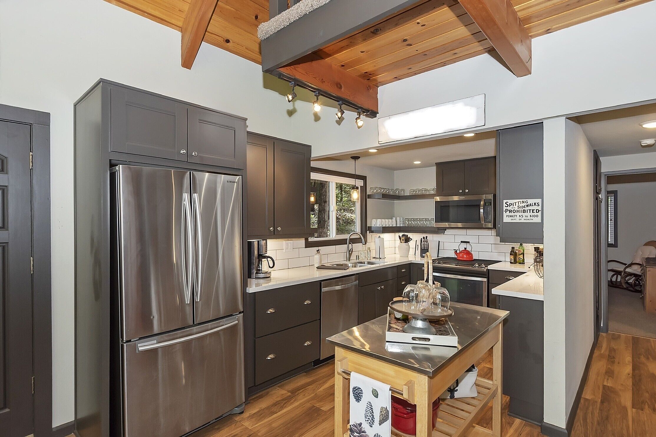 A modern kitchen with stainless steel appliances, wooden ceiling beams, and a view of a sidewalk.
