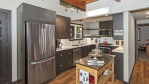 Une cuisine moderne dotée d’appareils électroménagers en acier inoxydable, de meubles de rangement aux couleurs sombres et d’un plafond en bois.