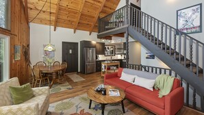 Un vaste espace de vie doté d’un haut plafond, de poutres en bois, d’une table à manger, d’un canapé rouge et d’un escalier menant à un niveau supérieur.