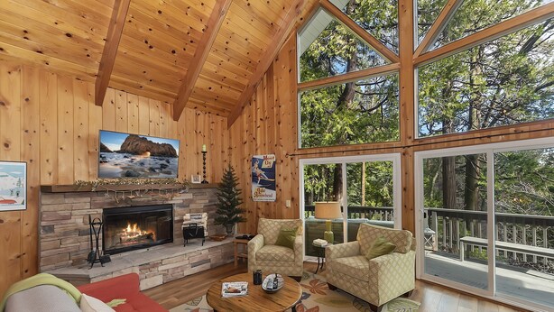 Un intérieur de chalet chaleureux avec une cheminée, de grandes fenêtres et une terrasse.