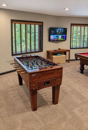 A room with a foosball table, a pool table, and a television displaying a movie.