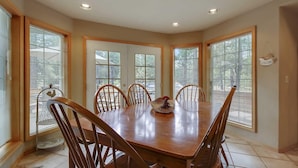 Comedor con mesa y sillas de madera, ventanas amplias con persianas y puerta que da al exterior.