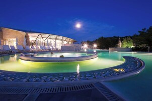 Zona de piscina con sillones de descanso y un edificio con fachada de vidrio.