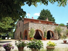 Un edificio de piedra con arcos, rodeado de plantas en macetas y árboles.