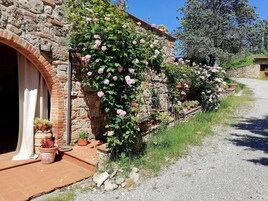 Un edificio rústico de piedra con un arco de ladrillo, un camino de grava y un exuberante jardín de rosas.