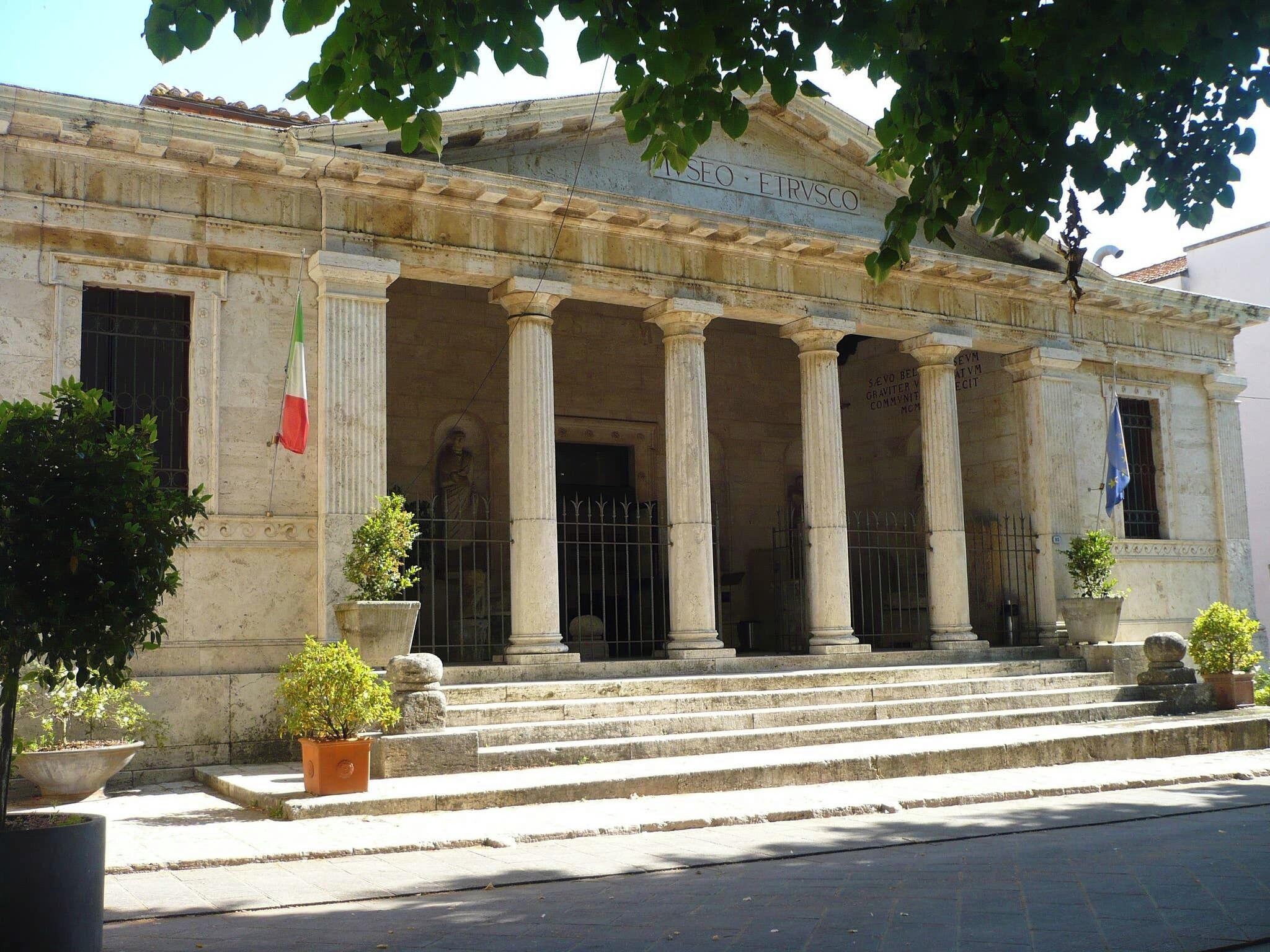 A classical building with columns, a flag, and steps leading to the entrance.