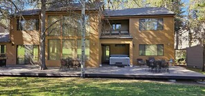 Ein zweistöckiges Haus mit einer Terrasse, Sitzgelegenheiten im Freien und einem Grill.