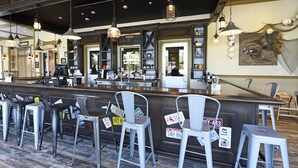 A restaurant interior with a bar area, metal chairs, and hanging lights.