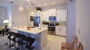 A modern kitchen with white cabinets, a central island, stainless steel appliances, and pendant lighting.
