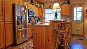 A kitchen with wooden cabinets, stainless steel appliances, a microwave, and a bar stool area. - Modoc 05 (Bend)