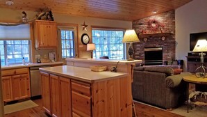 A kitchen with wooden cabinets, a central island, a dining area with a sofa, and a fireplace. - Modoc 05 (Bend)