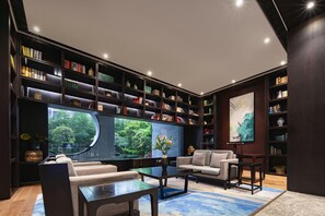 Un salon moderne avec une grande bibliothèque, un canapé, une table basse et une grande fenêtre donnant sur un paysage verdoyant.