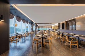 A restaurant with wooden tables and chairs, large windows, and a view of the outdoors.