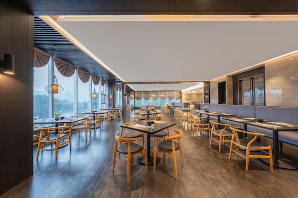 Un restaurant avec des tables et des chaises en bois, de grandes fenêtres et une vue sur l’extérieur.