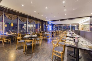 A restaurant with multiple tables and chairs, a kitchen area, and large windows.