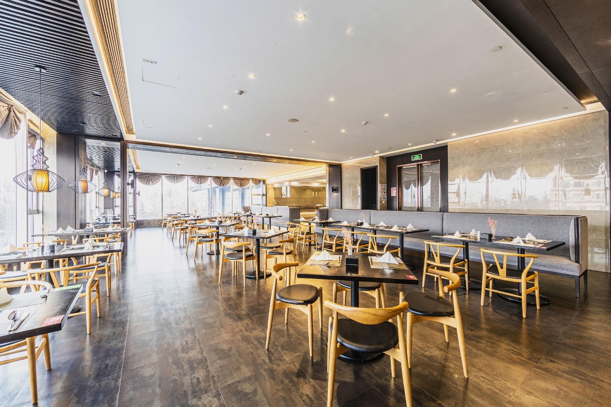 A spacious restaurant with multiple dining tables and chairs, a modern ceiling design, and large windows allowing natural light.