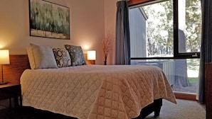 A bedroom with a large bed, two bedside lamps, a painting on the wall, and a window with curtains. - Meadow House 21 (Bend)