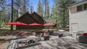 A wooden deck with outdoor furniture, red umbrellas, and a barbecue grill. - Conifer 10 (Bend)