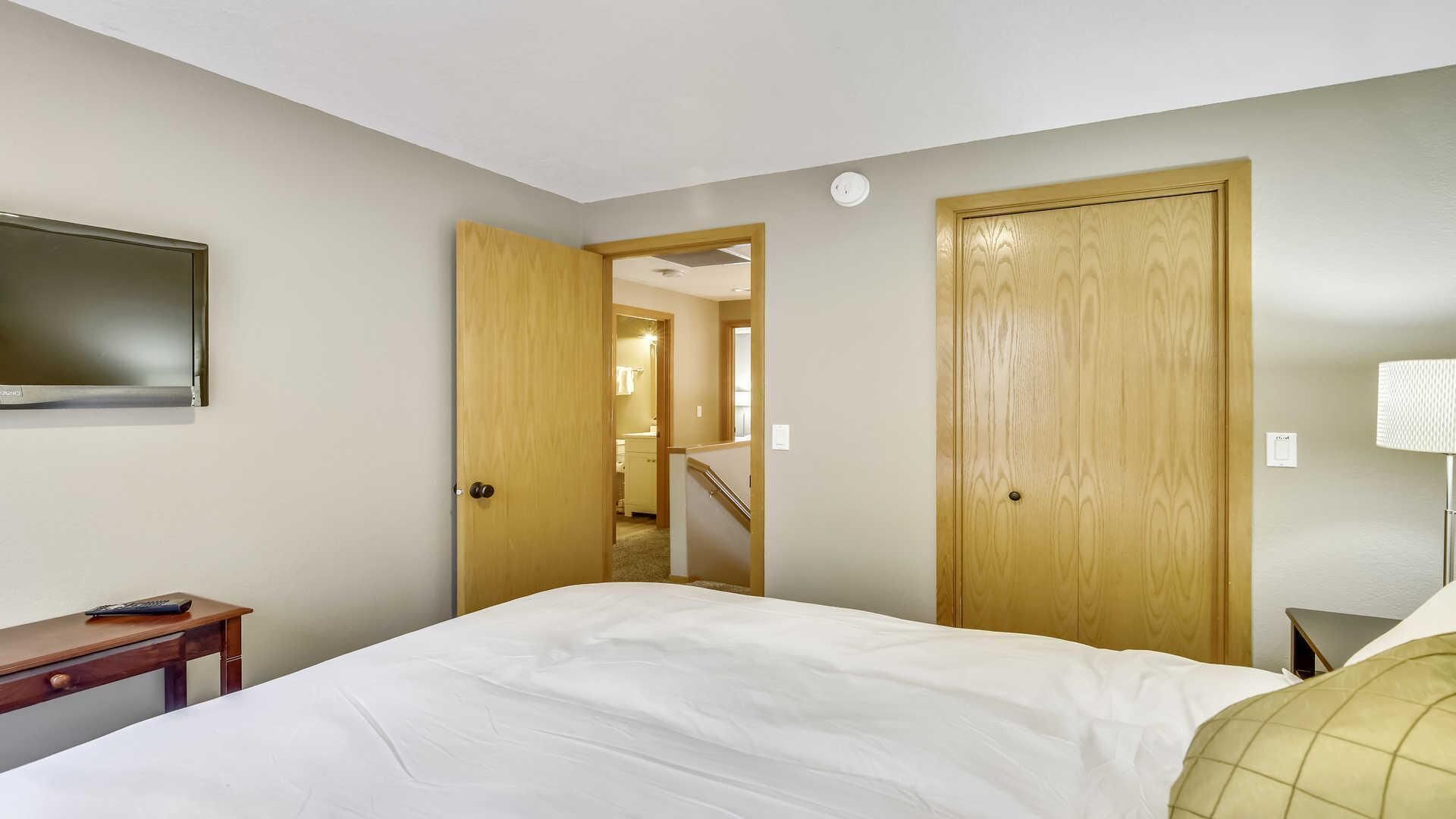 A hotel room with a bed, a desk, a TV, and a door leading to a staircase.