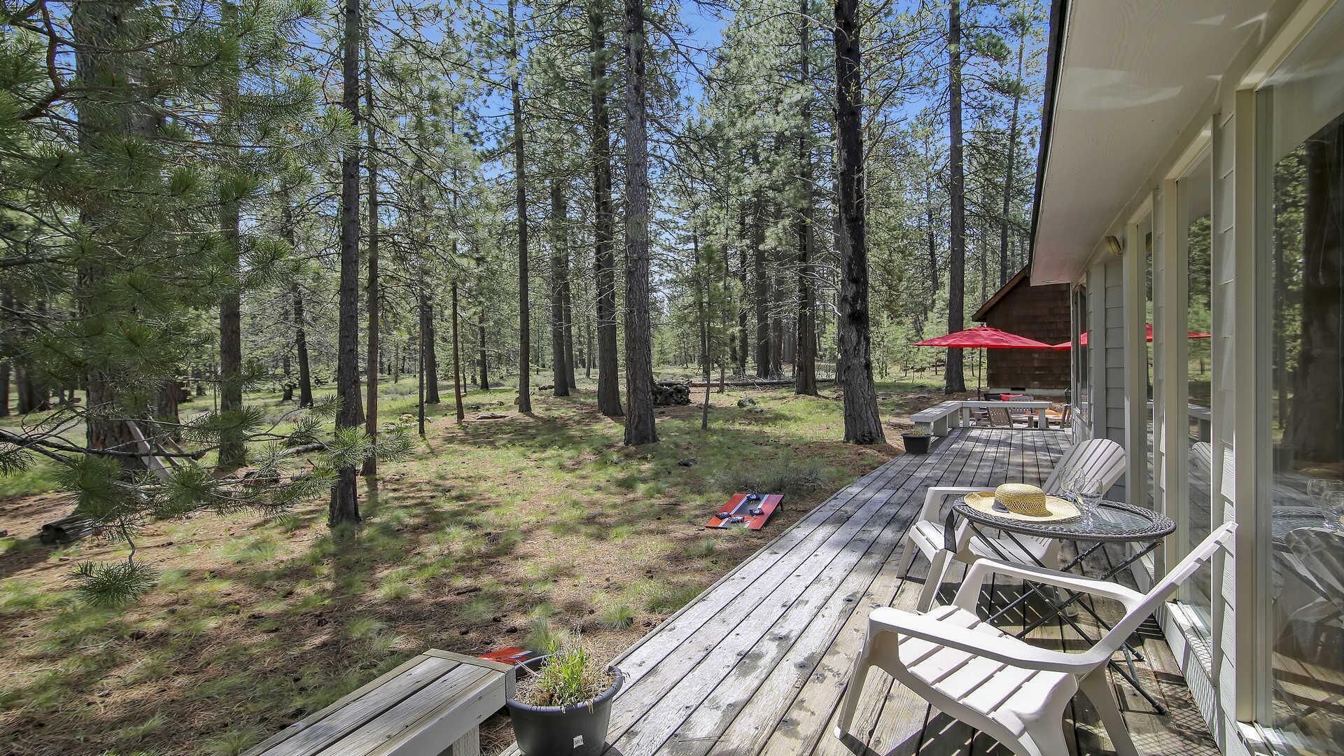A wooden deck with outdoor furniture, surrounded by a forest.