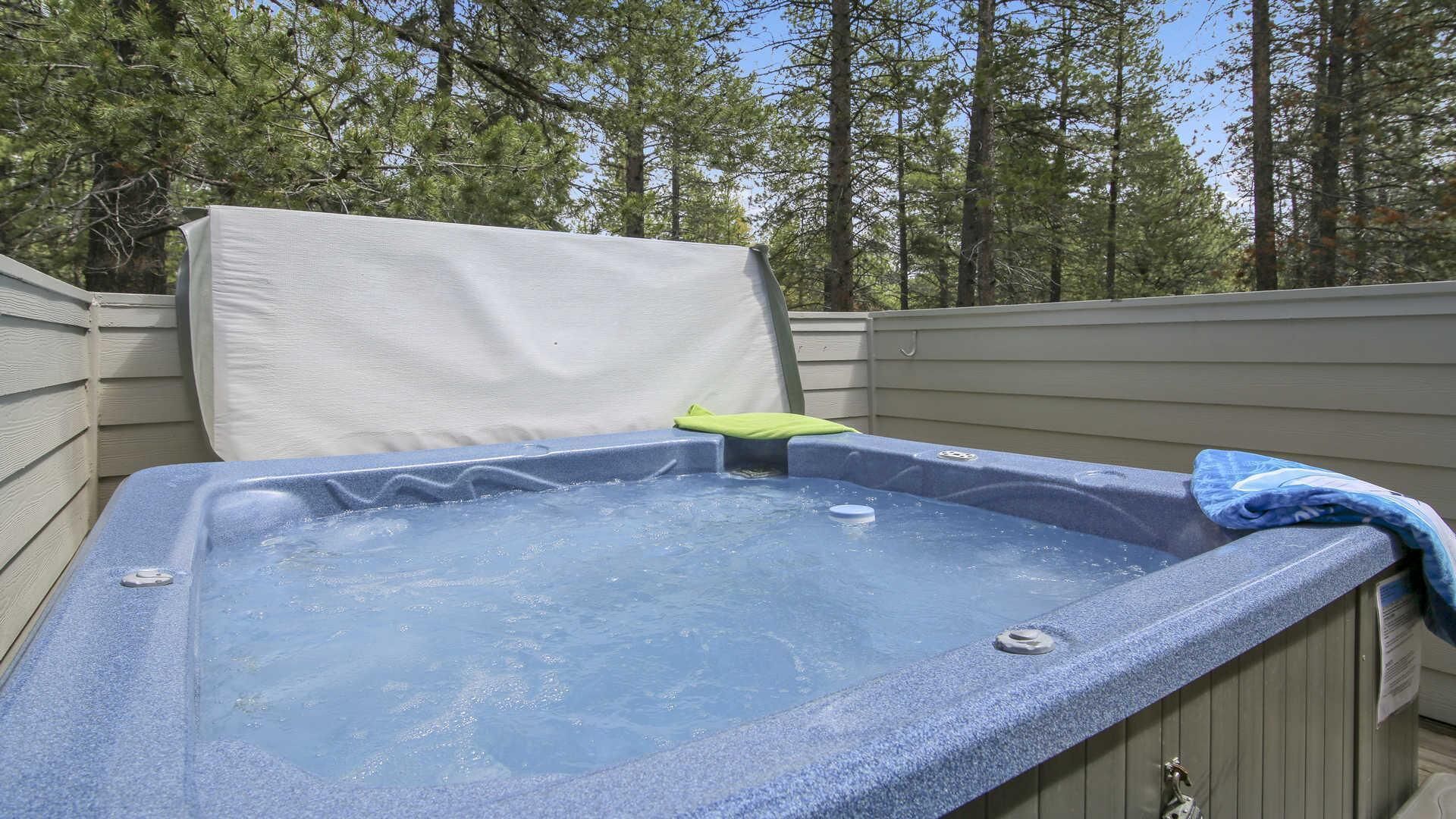 A hot tub with a white cover, surrounded by wooden deck and trees.