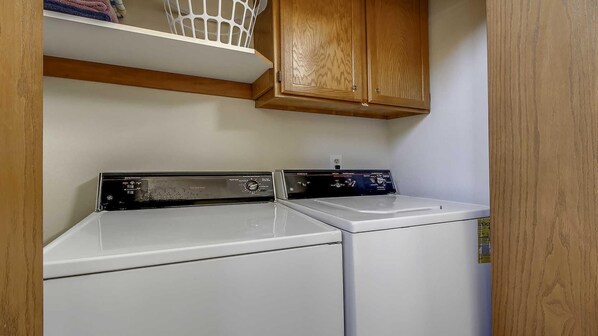 A laundry area with two stacked washers and dryers, wooden cabinets above, and a basket on the shelf.