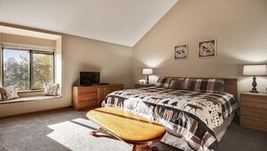 A bedroom with a large bed, a bench, a dresser, a television, and two wall-mounted lamps. - Skyline Condo 02 (Bend)