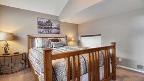 A bedroom with a wooden bed, two bedside tables, a painting on the wall, and a window with shutters. - Powder Village E2 (Bend)