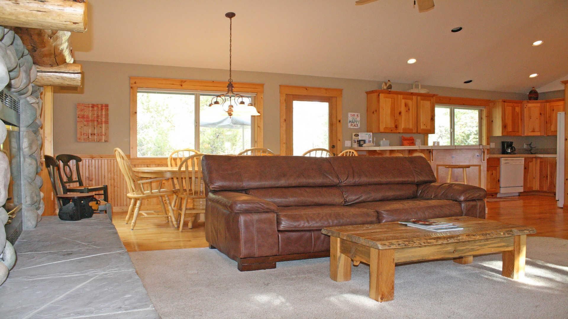 A cozy living room with a leather sofa, wooden coffee table, and a dining area with wooden chairs and a table.