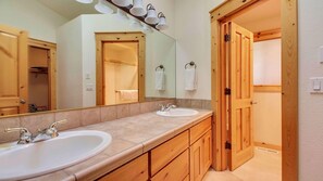 A bathroom with two sinks, wooden cabinets, a large mirror, and a wooden door. - Quail 5 (Bend)