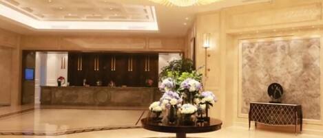 A lobby with a reception desk, a chandelier, and a decorative table with flowers.