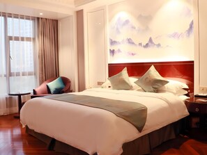 Una habitación de hotel con una cama grande, cabecera roja y una obra de arte en la pared que muestra montañas.