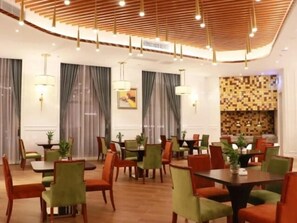 A hotel dining area with multiple tables and chairs, wooden ceiling with hanging lights, and a patterned wall in the background. - Greentree Eastern Yancheng Binhai County Aobaolia Beichen Hotel (Yancheng)