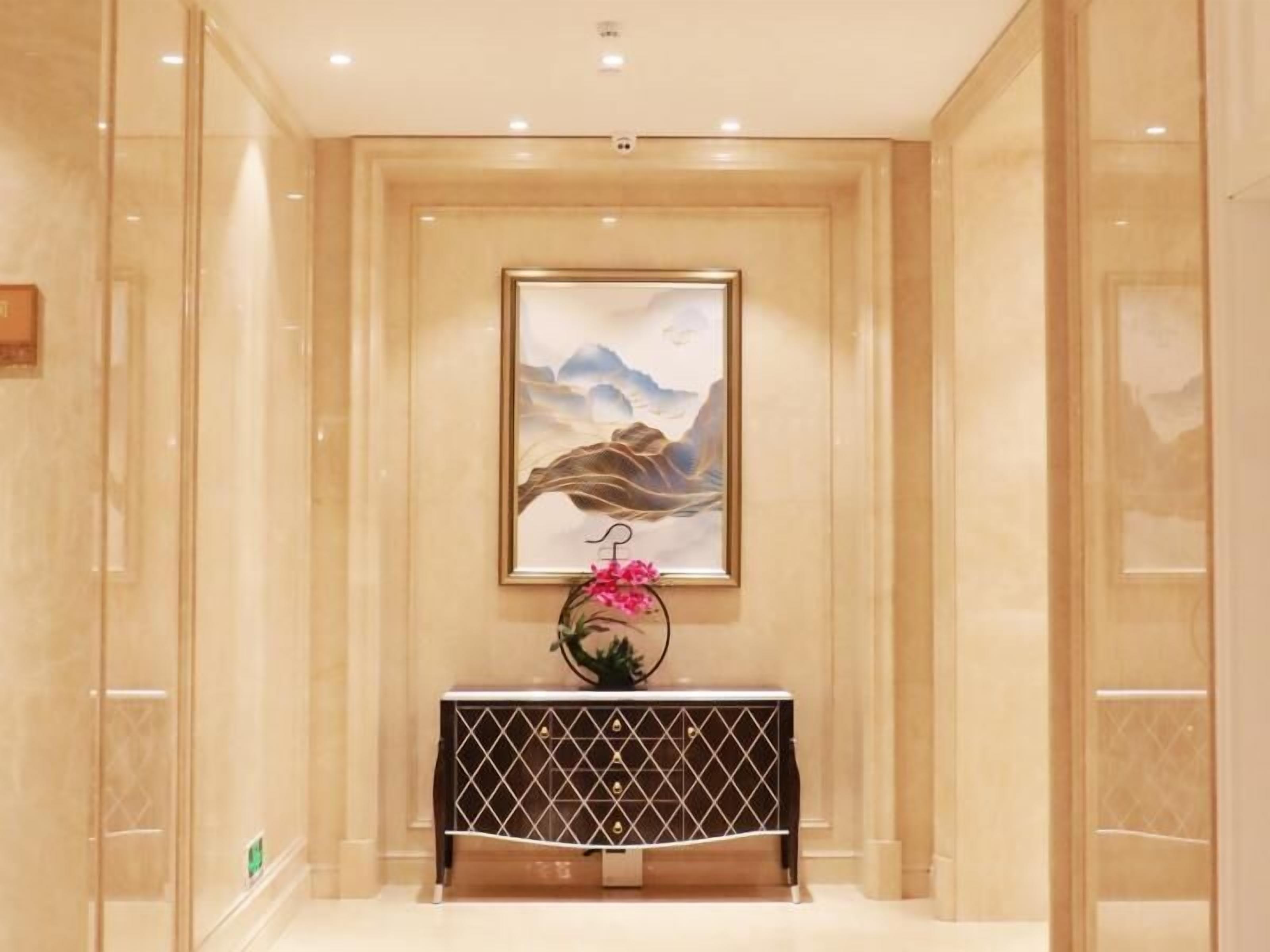 A hallway with a framed artwork on the wall, a console table with a geometric pattern, and a pink flower arrangement.