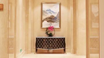 A hallway with a framed artwork on the wall, a console table with a geometric pattern, and a pink flower arrangement.