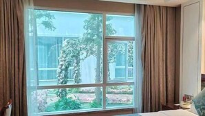 A hotel room with a large window, a bed with a patterned bedspread, wooden flooring, and curtains. - Greentree Eastern Yancheng Binhai County Aobaolia Beichen Hotel (Yancheng)