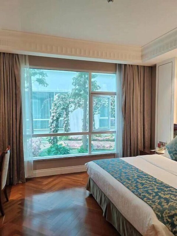 Ein Hotelzimmer mit großem Fenster, einem Bett mit gemustertem Überwurf, Holzboden und Vorhängen.