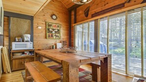 Ein gemütliches Blockhaus-Interieur mit einem Holztisch, Bänken, einer Küchenzeile mit Mikrowelle und einem großen Fenster mit Jalousien.
