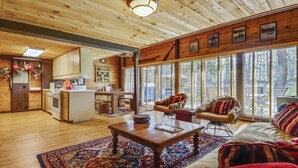Ein gemütliches Blockhaus-Interieur mit Holzvertäfelung, einer Küche, einem Essbereich und großen Fenstern.