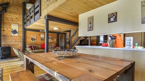 Ein rustikales Blockhaus-Interieur mit einem Holzesstisch, einem Metallkorb, einer Couch mit roten Kissen und einer Treppe.
