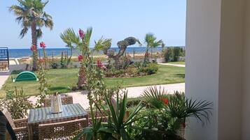 A balcony with a view of the sea, a garden with palm trees, and a patio area with wicker furniture.