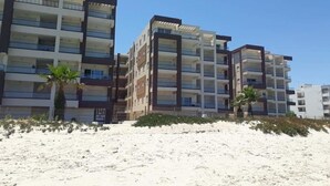 Een strandhotel met meerdere verdiepingen, balkons en een zandstrand op de voorgrond.
